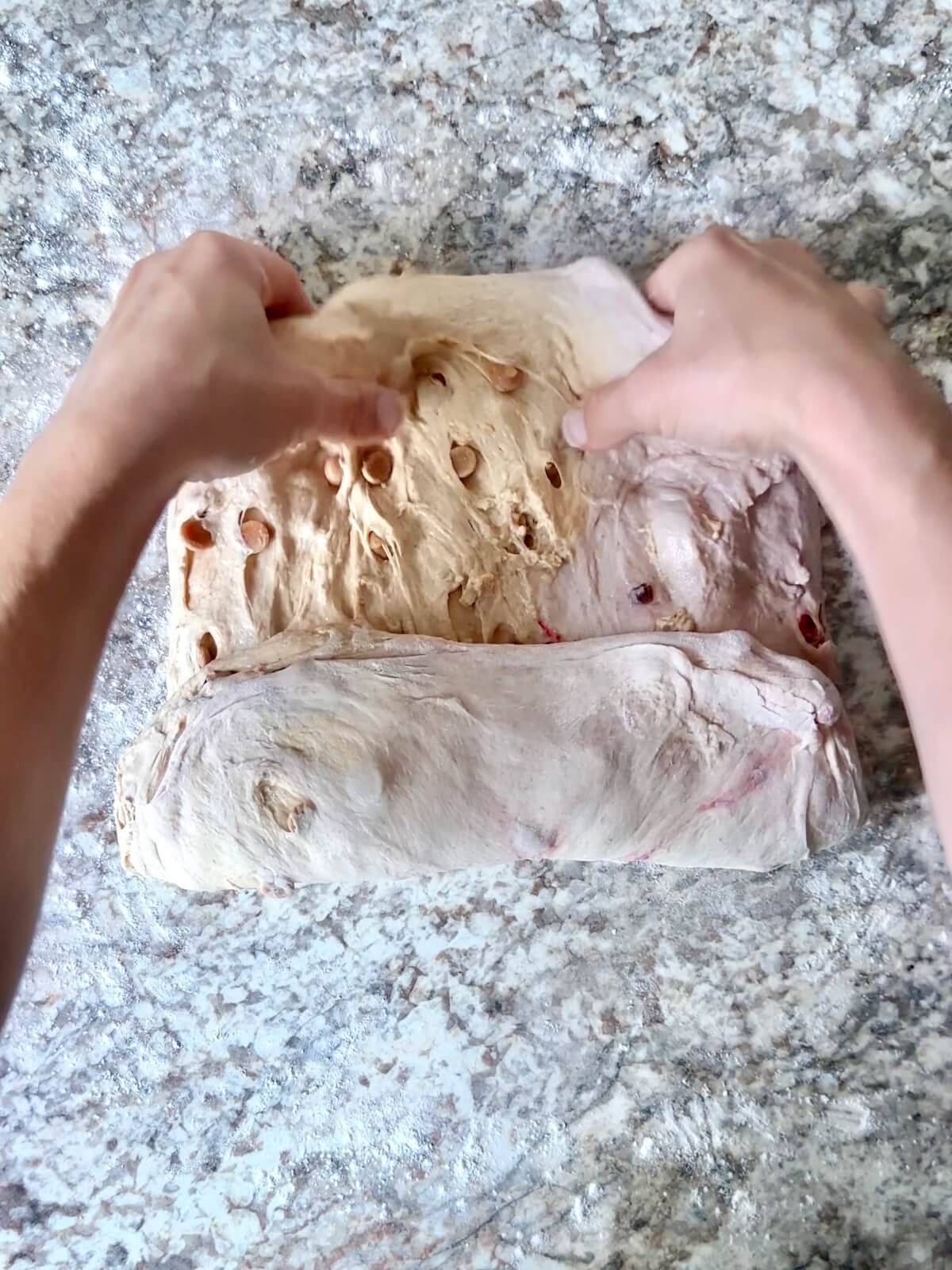 Two hands shaping the dough on a lightly floured counter.