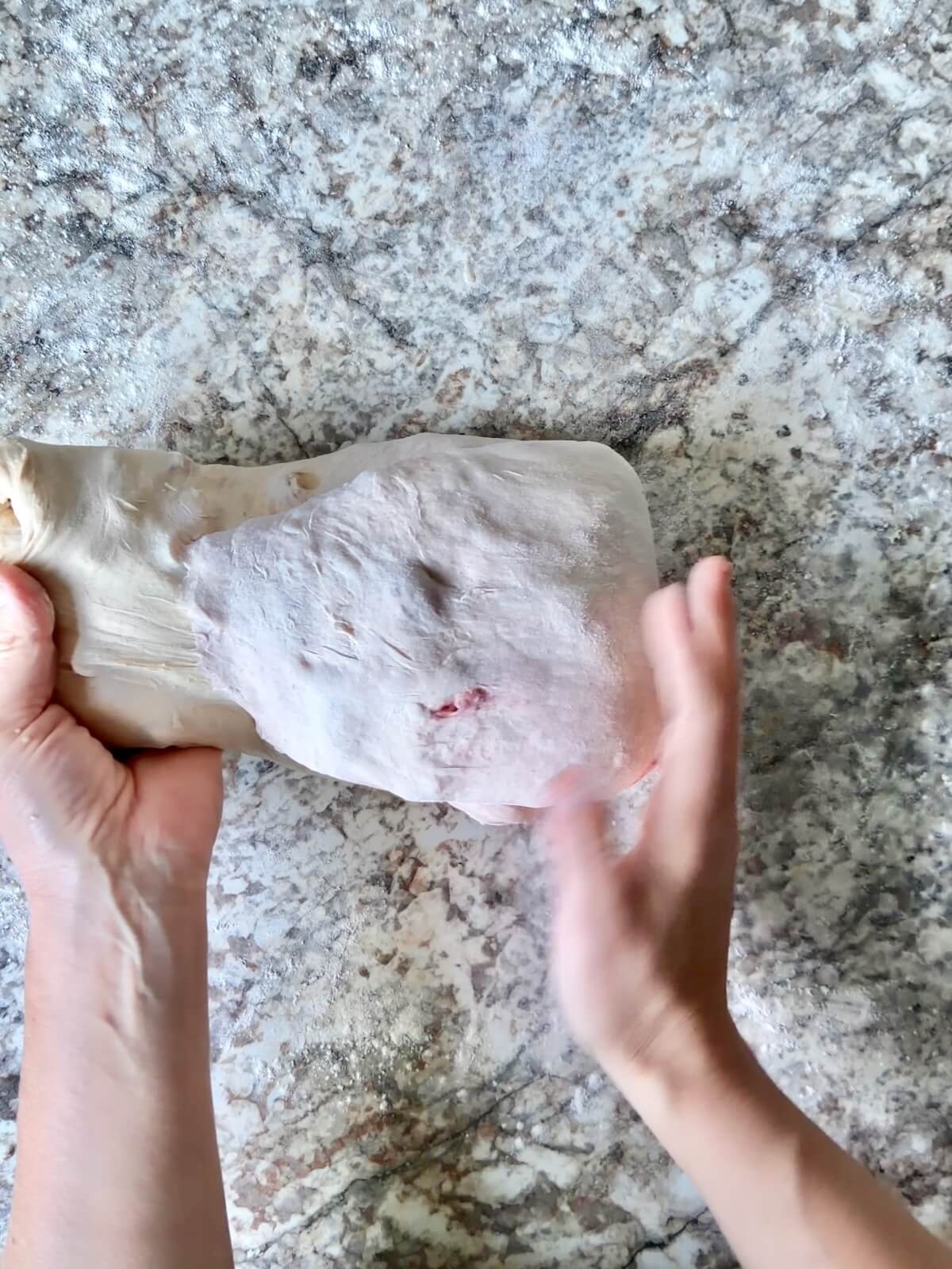 Two hands shaping the dough on a lightly floured counter.