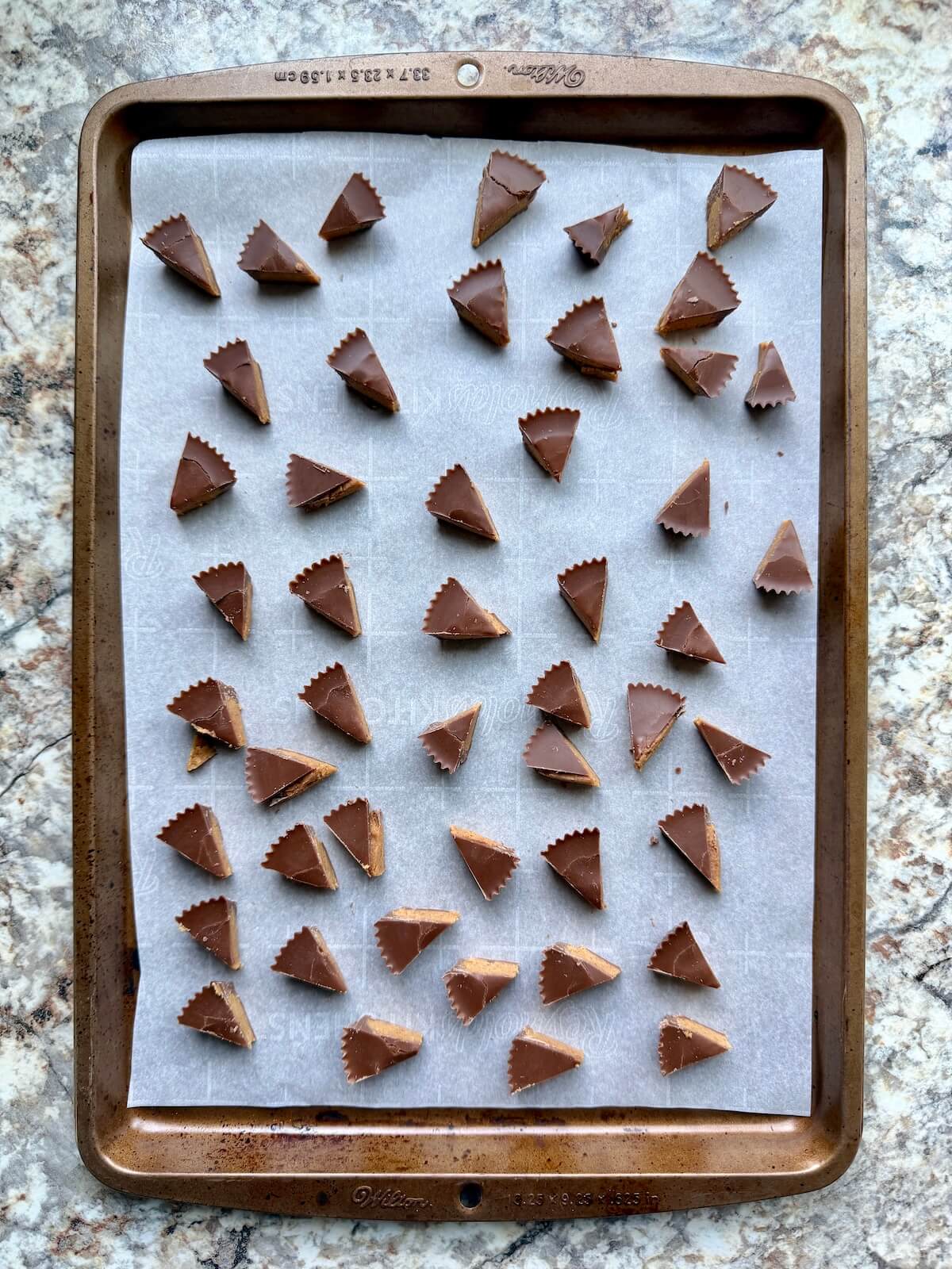 Reese's peanut butter cups cut into pieces on a parchment-lined baking sheet.