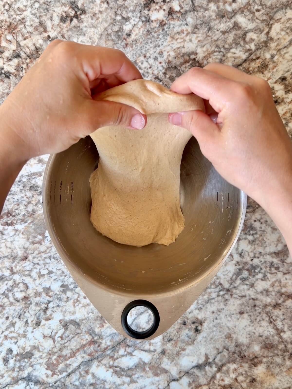 Two hands stretching and folding the peanut butter portion of dough in a mixing bowl.