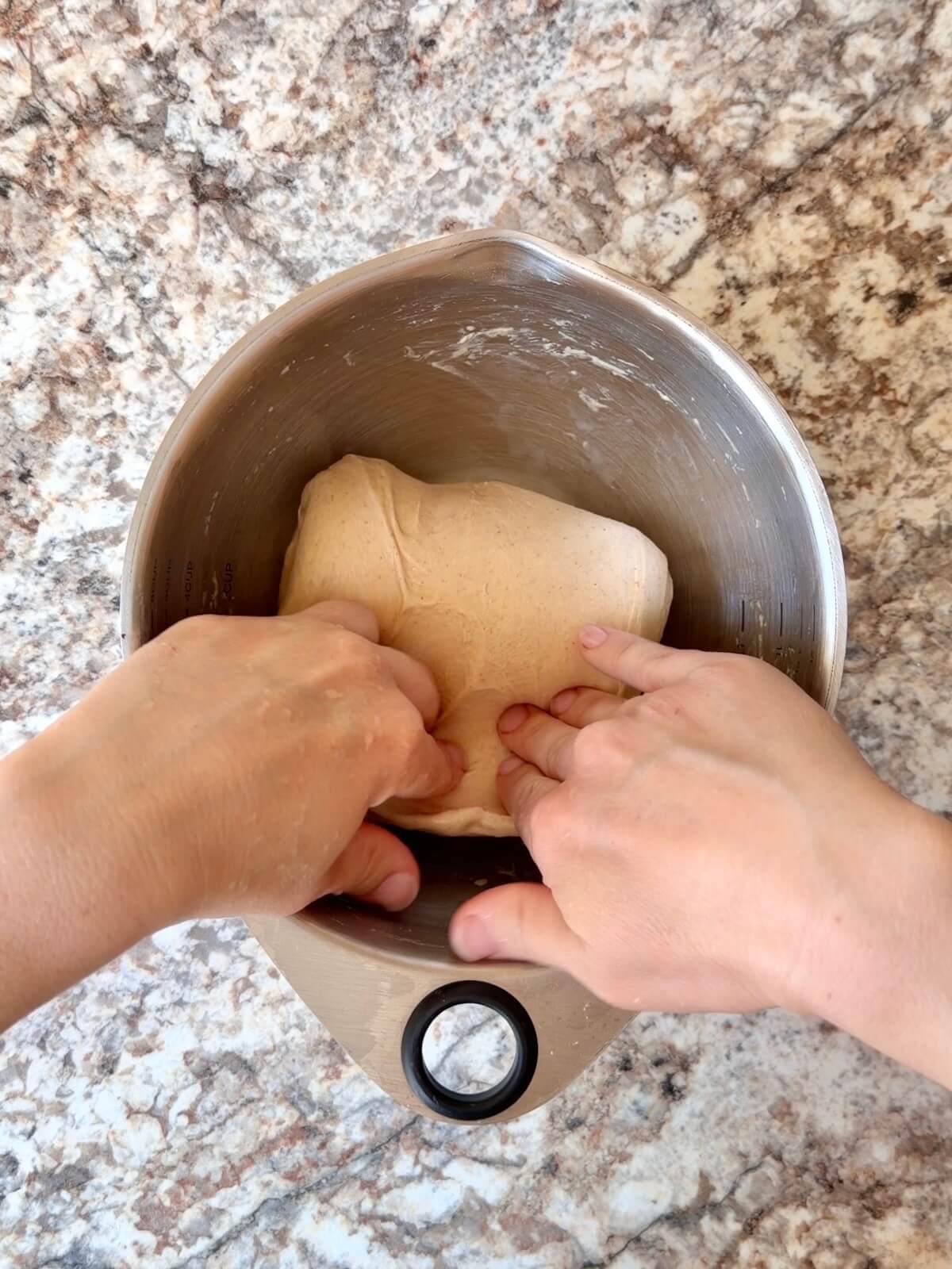 Two hands stretching and folding the peanut butter portion of dough in a mixing bowl.