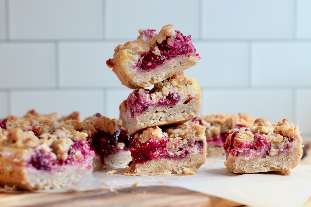 A stack of three sourdough raspberry cheesecake bars with more bars on the counter surrounding it.