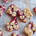 Several sourdough raspberry cheesecake bars on a piece of parchment paper.