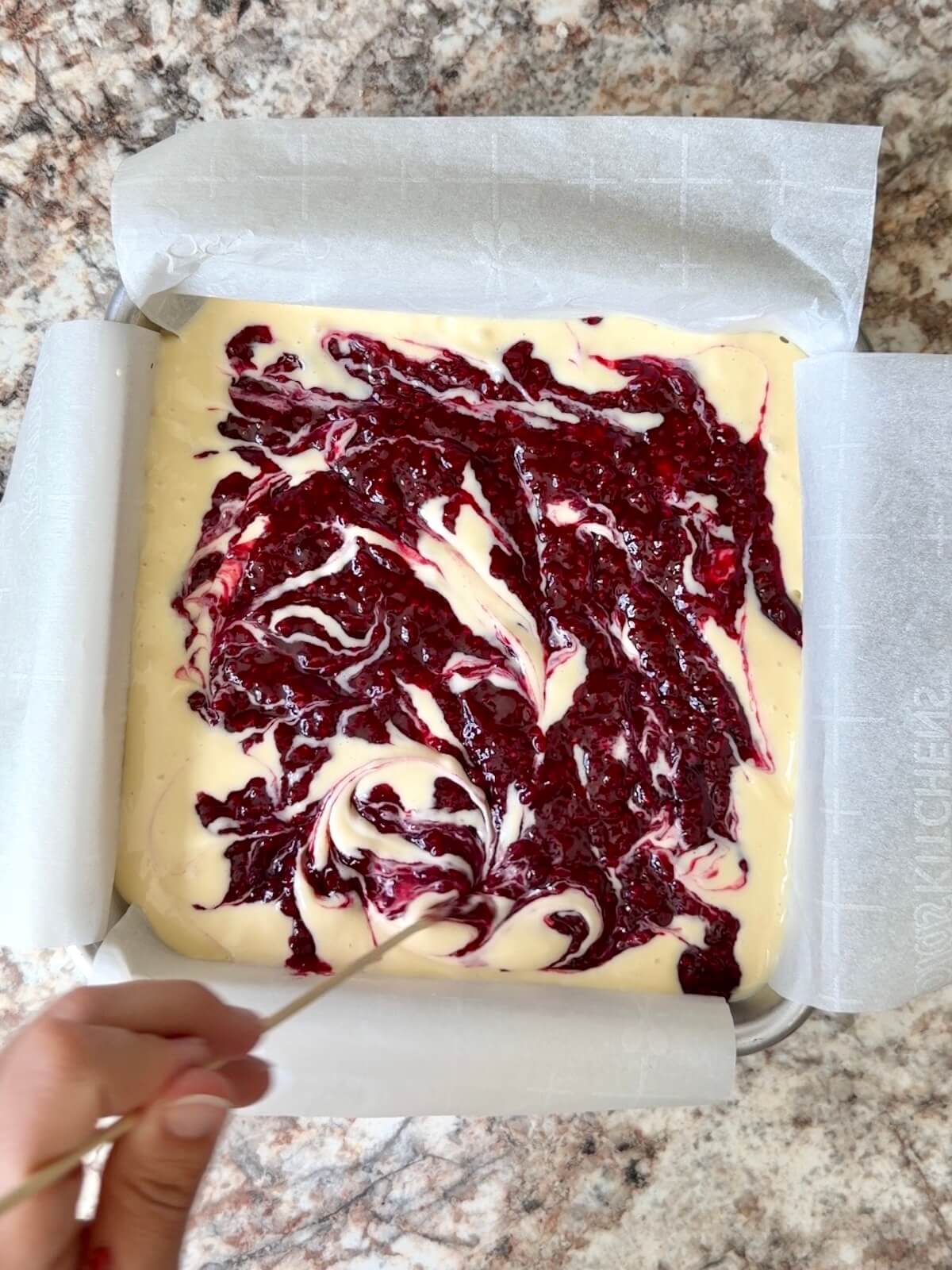 The raspberry layer being swirled into the cheesecake layer.