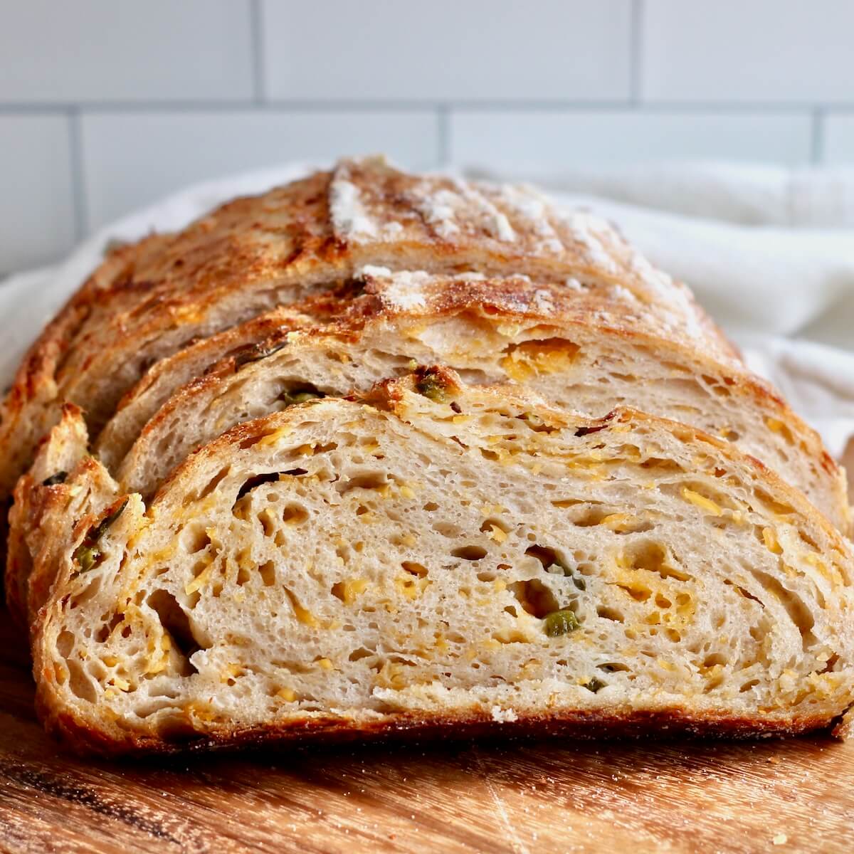 A sliced loaf of jalapeño cheddar sourdough bread on a wooden cutting board.