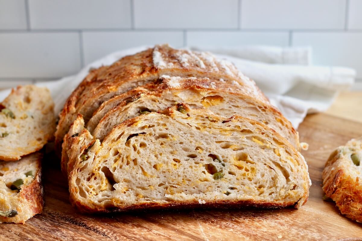 A sliced loaf of jalapeƱo cheddar sourdough bread on a wooden cutting board.