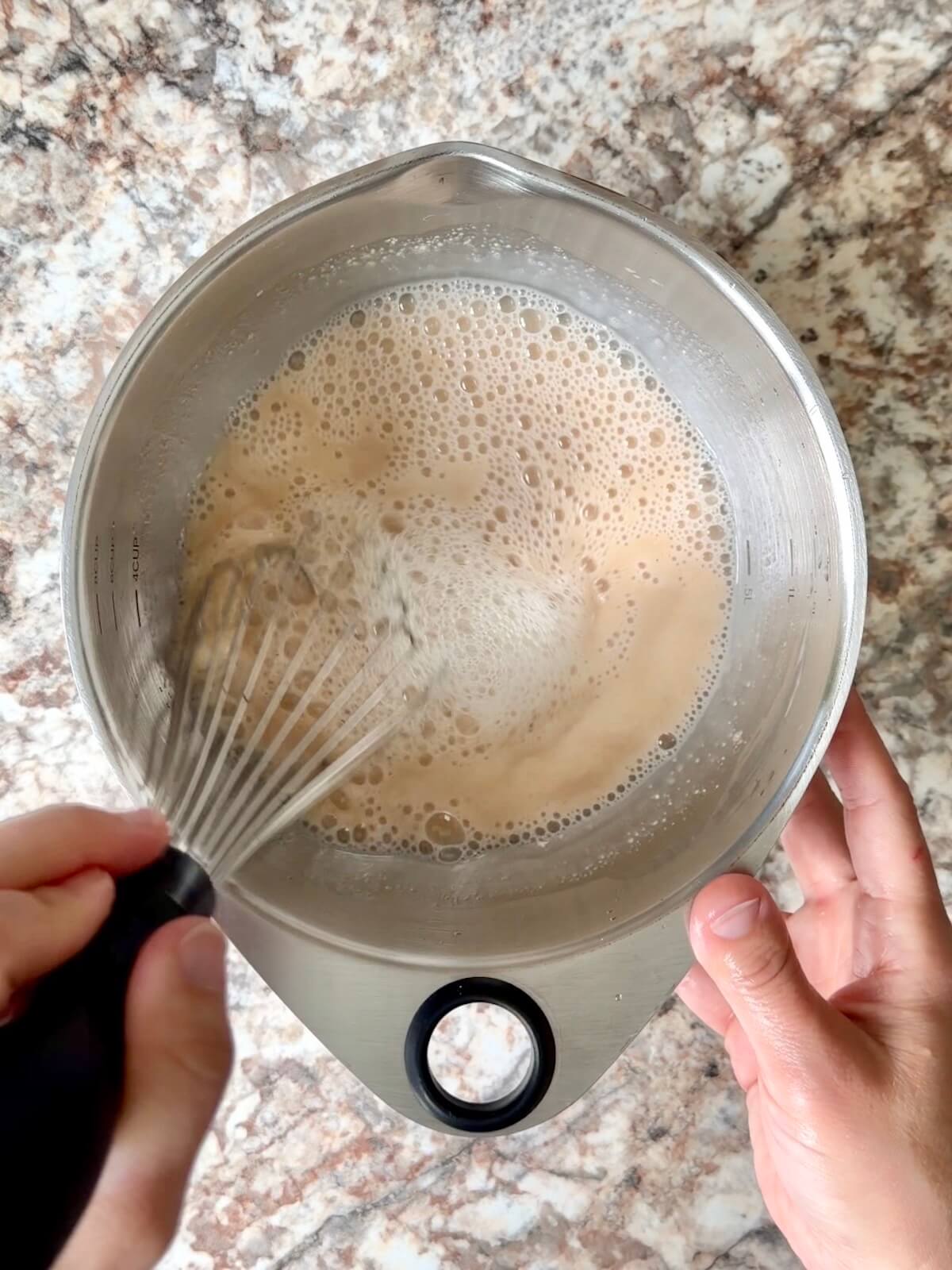 Water and sourdough starter being whisked together in a bowl.