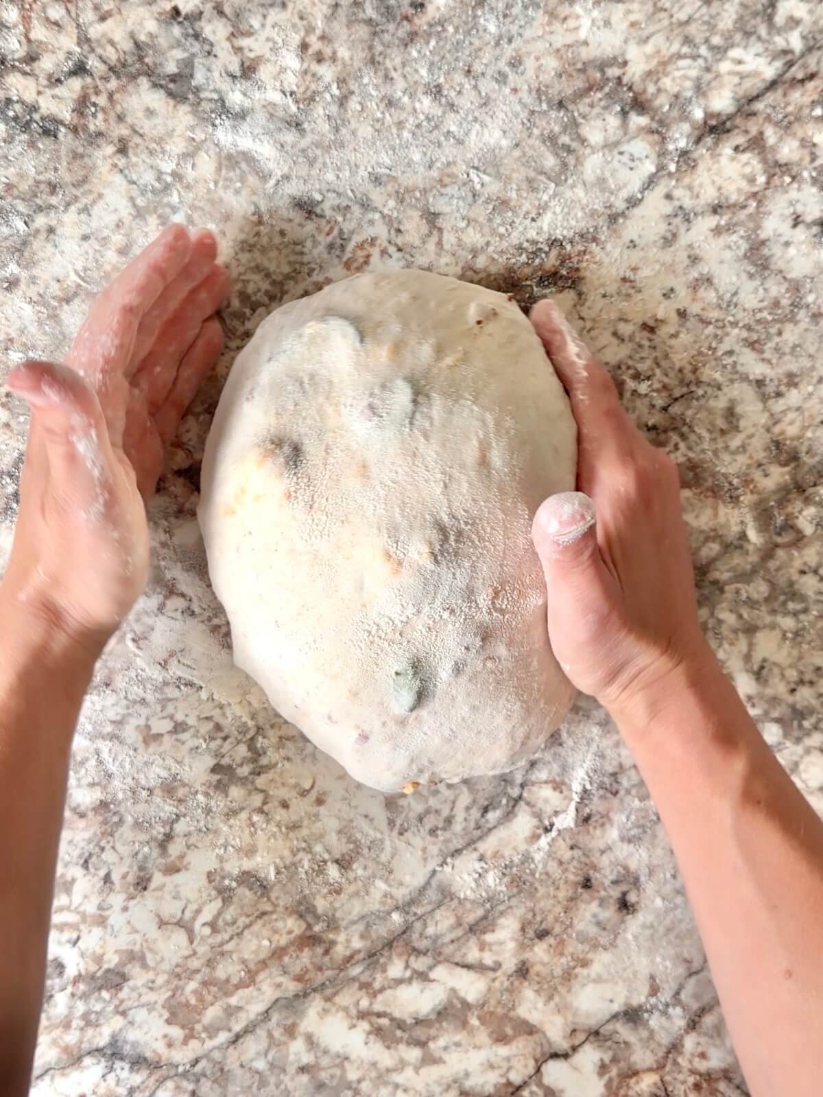 The dough being rounded into a ball by two hands.