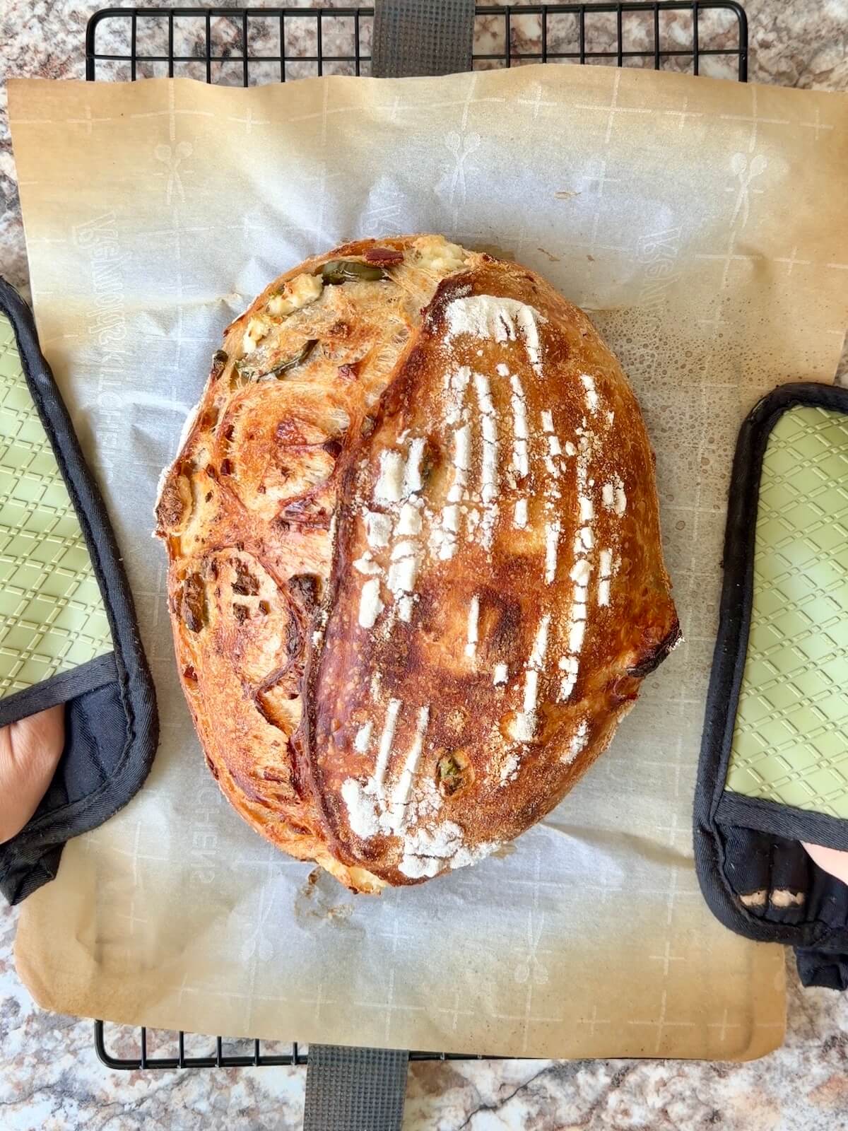 A baked loaf of jalapeƱo popper sourdough bread on a wire cooling rack.