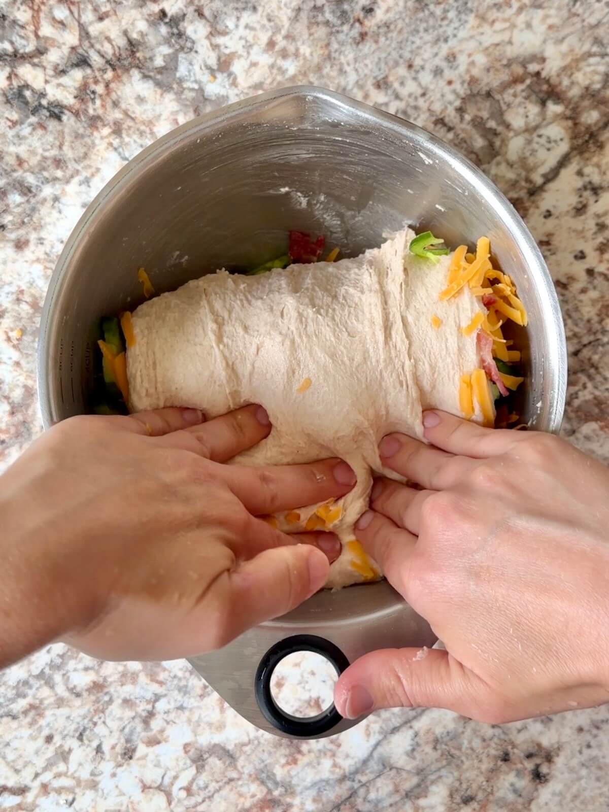 JalapeƱos, shredded cheddar, and bacon being folded into the dough in a bowl.