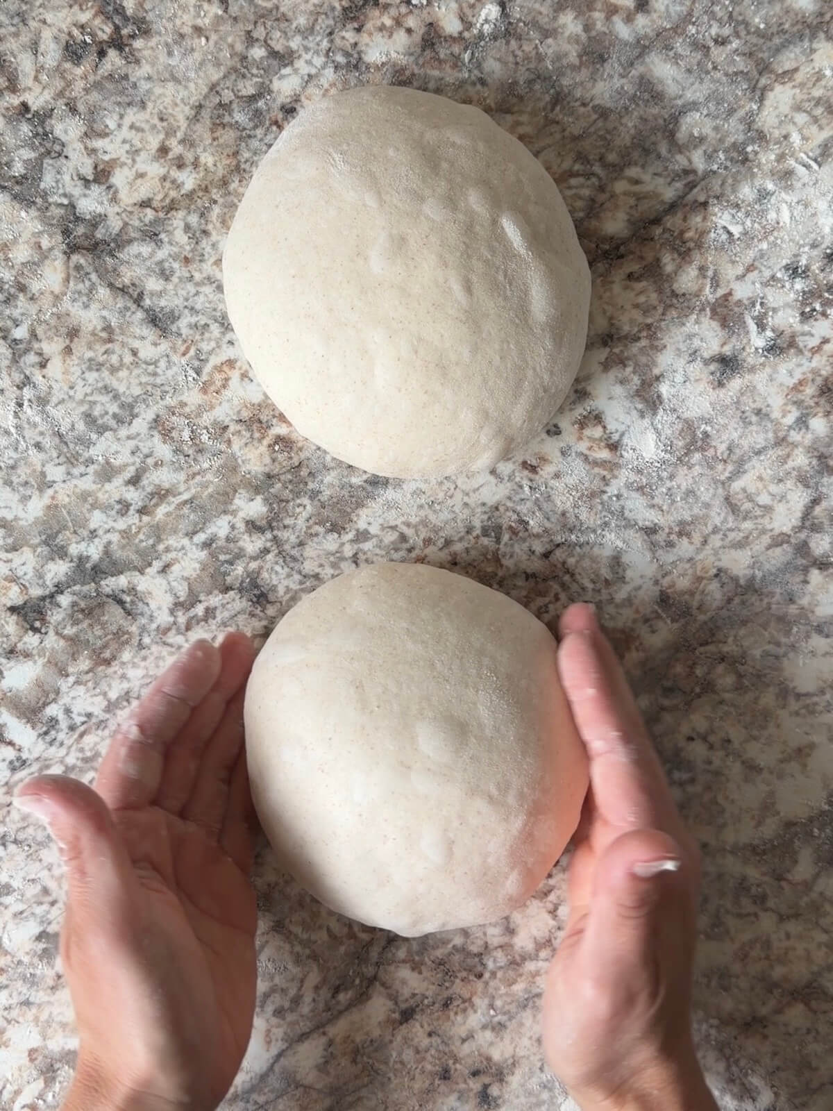 Sourdough bread dough being shaped into balls on a floured counter.