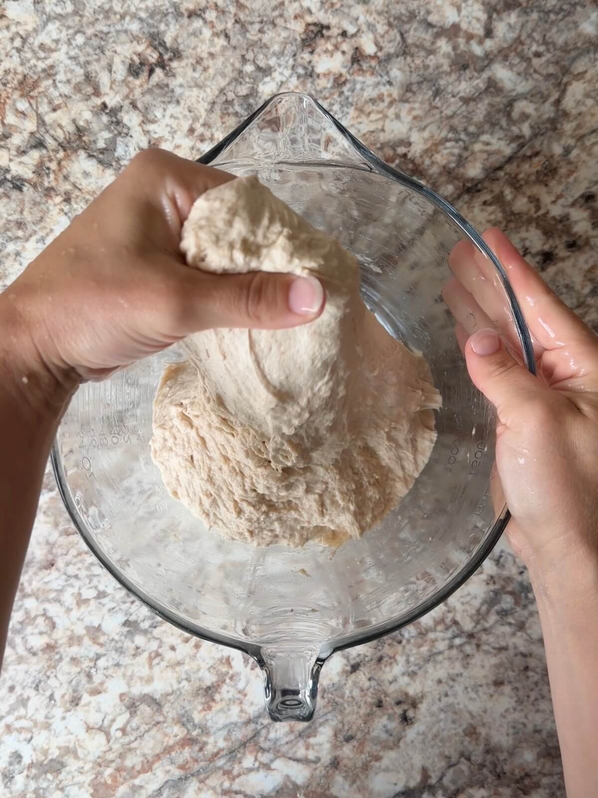 Sourdough bread dough being stretched and folded in a bowl.