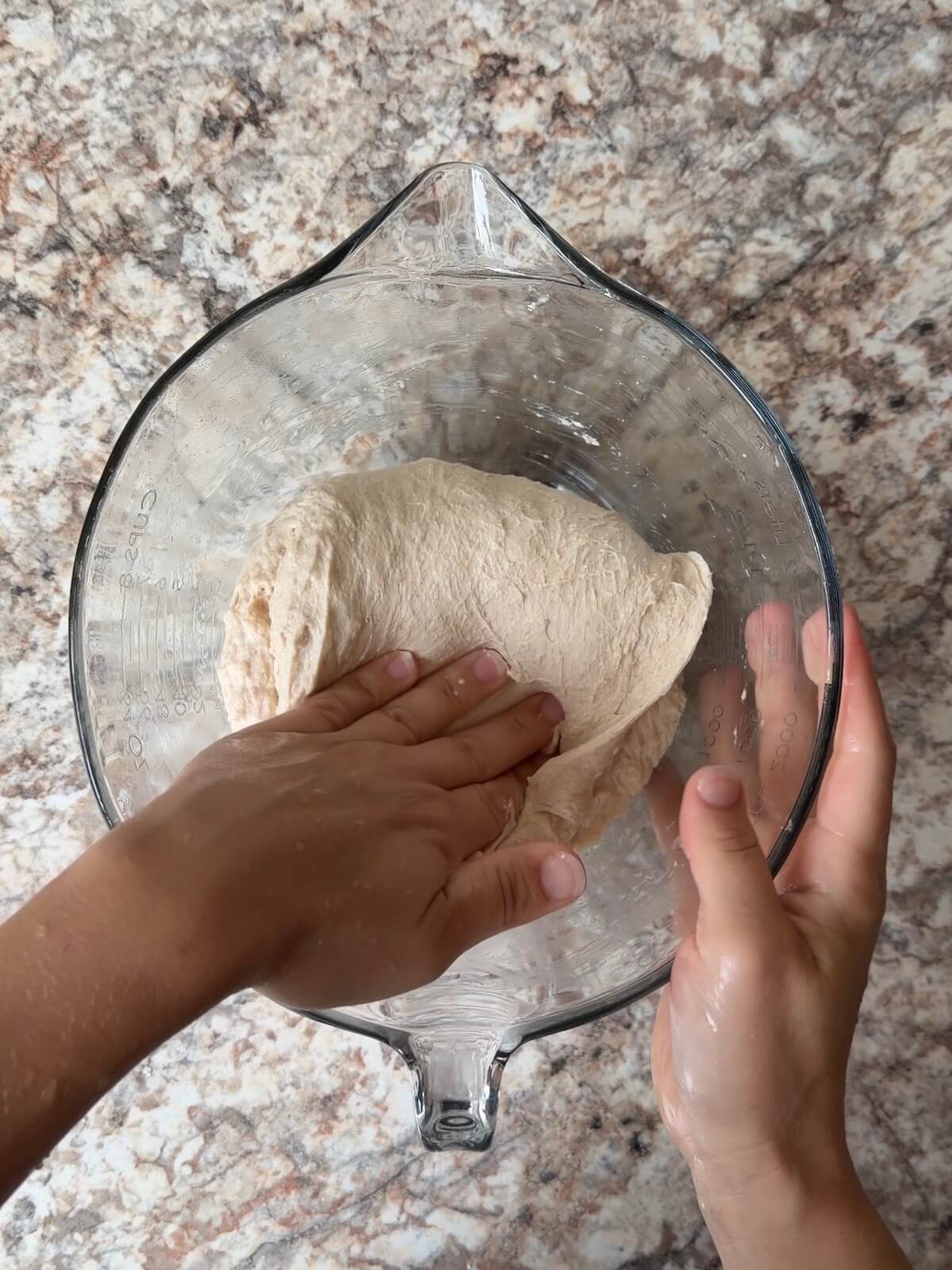 Sourdough bread dough being stretched and folded in a bowl.
