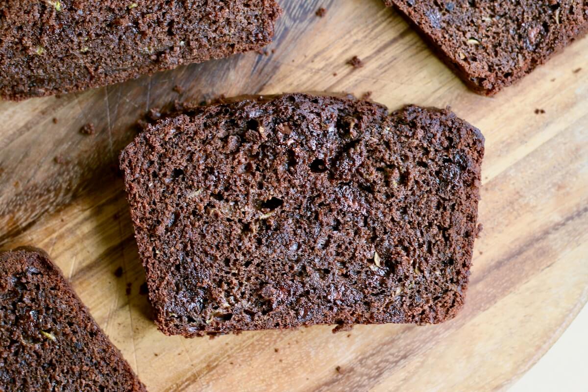 A slice of sourdough discard chocolate zucchini bread on a wooden cutting board.
