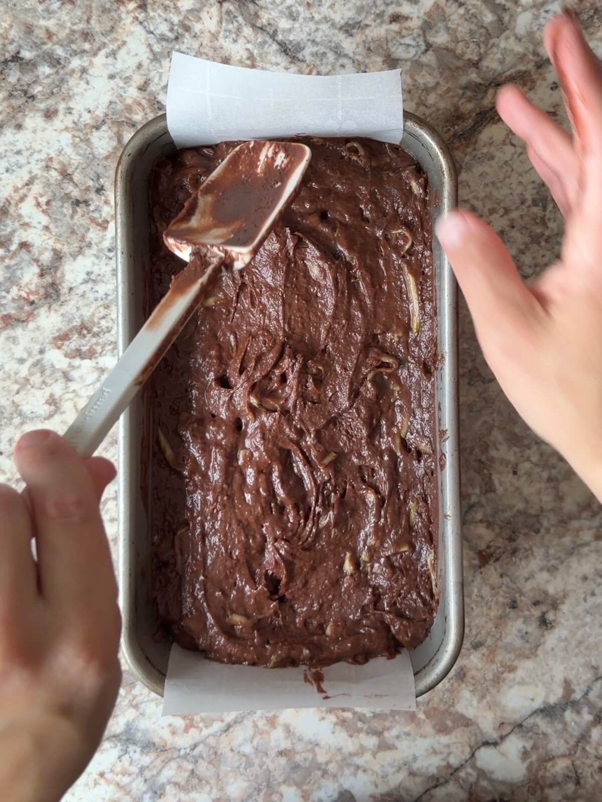 The chocolate sourdough zucchini bread being spread into a parchment-lined loaf pan.