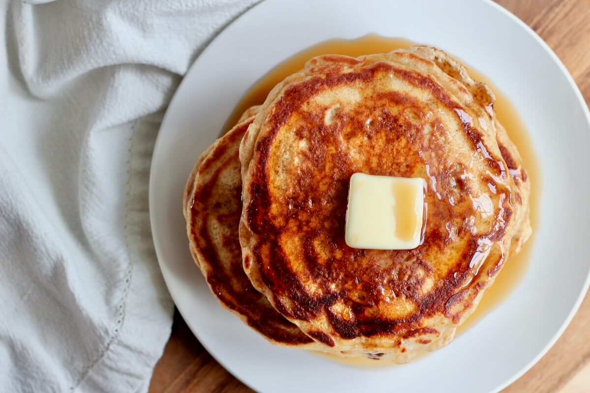 A stack of sourdough buttermilk pancakes with butter and maple syrup on a small plate.