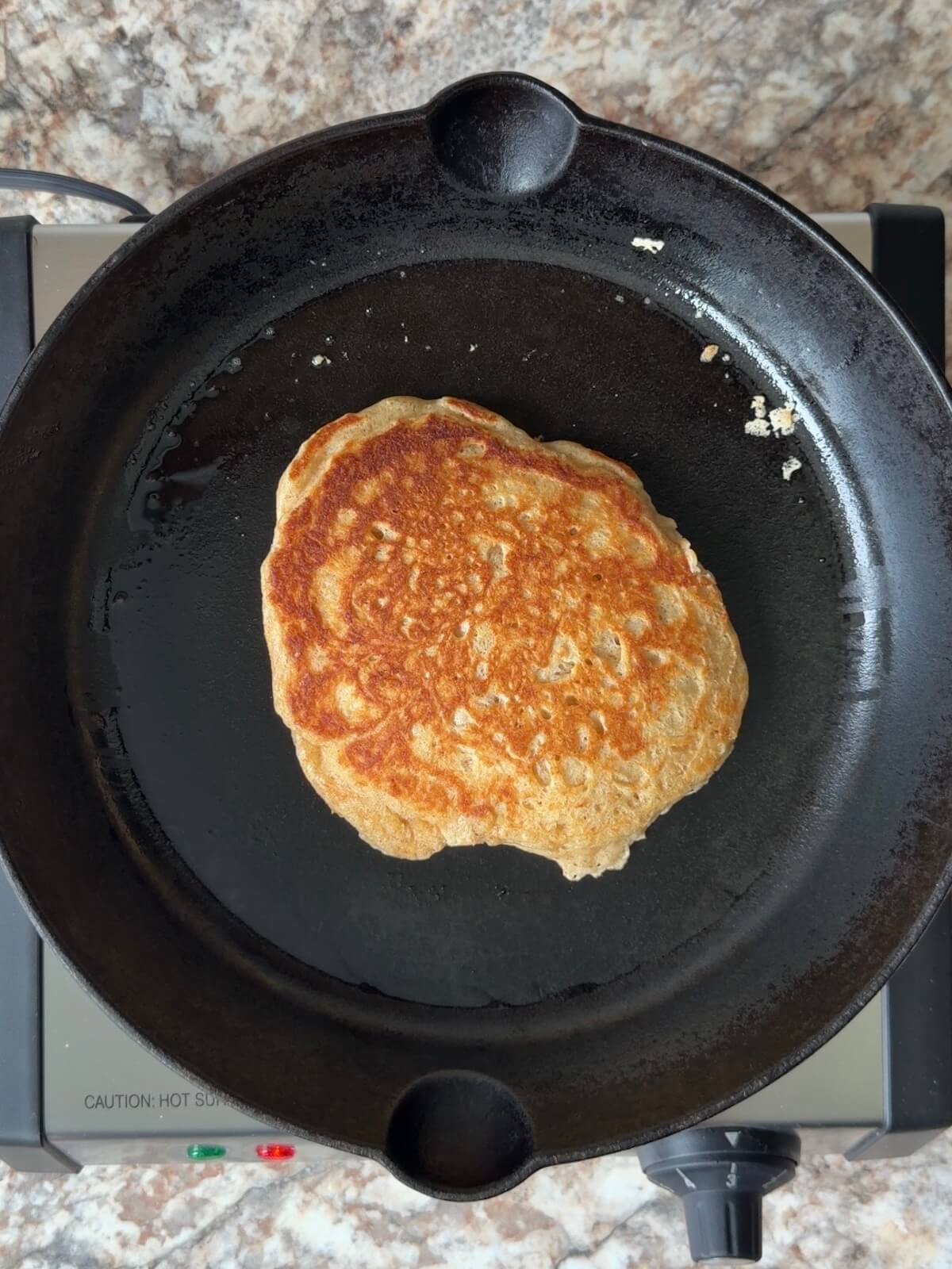 A golden brown sourdough pancake in a cast iron skillet.