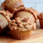 Several sourdough zucchini muffins with cinnamon streusel topping on a wooden counter.