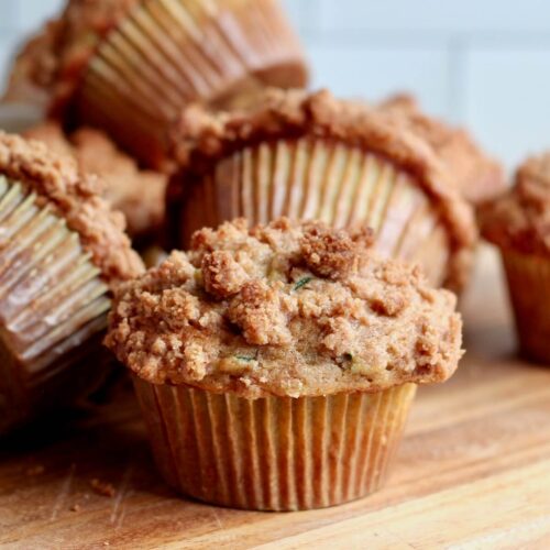 Several sourdough zucchini muffins with cinnamon streusel topping on a wooden counter.