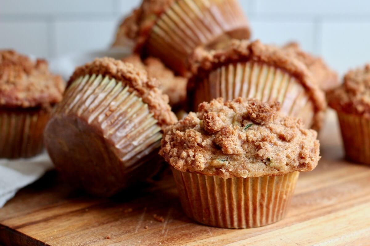 Several sourdough zucchini muffins with cinnamon streusel topping on a wooden counter.