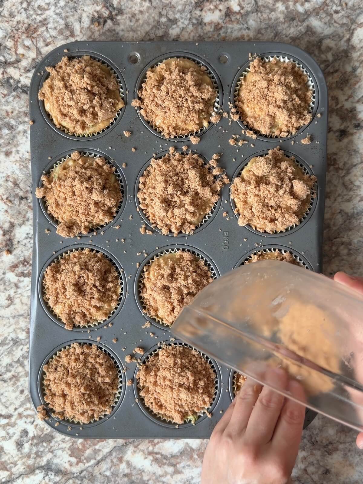 Cinnamon streusel being pressed on top of the sourdough zucchini muffins before baking.