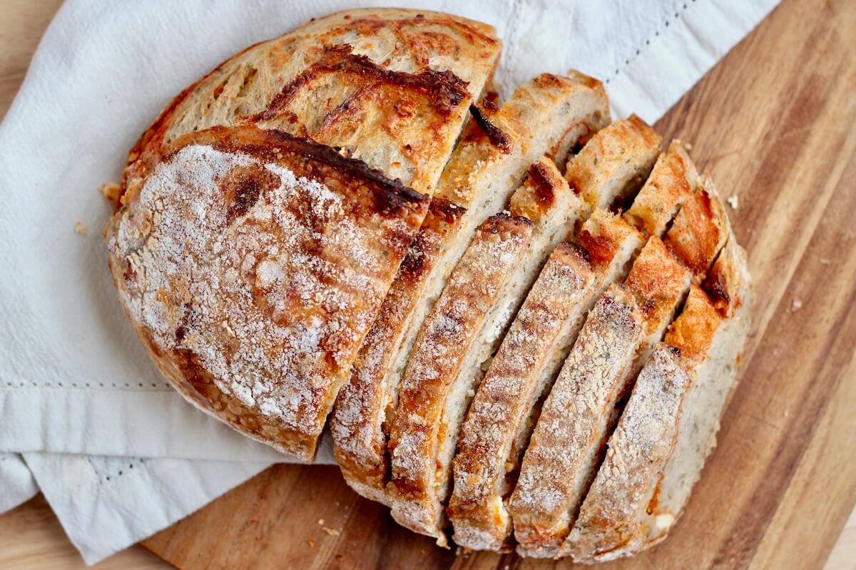 A half-sliced loaf of buffalo sourdough bread on a wooden cutting board with a white cloth napkin.