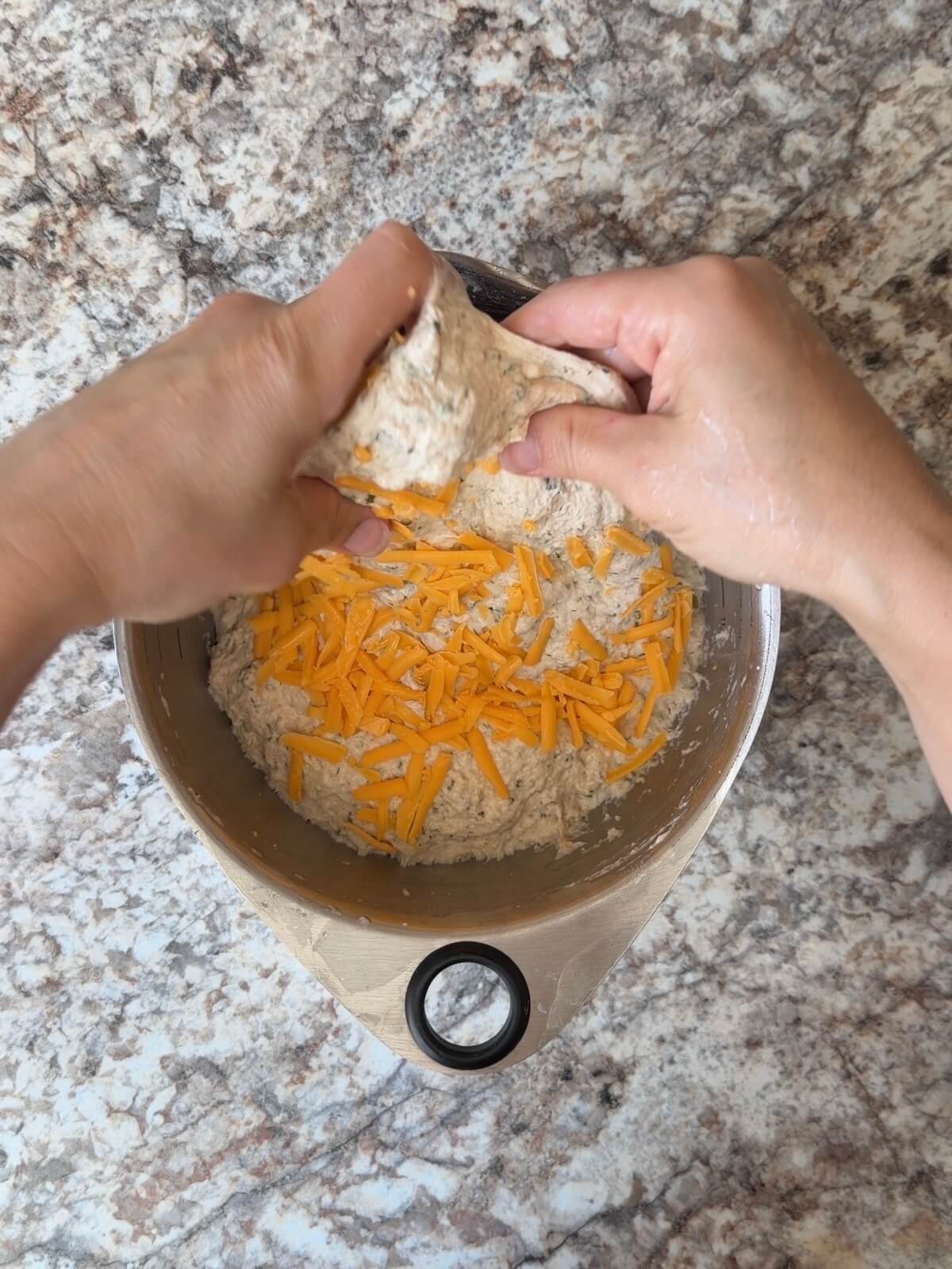 Shredded cheddar cheese being stretched and folded into the dough.