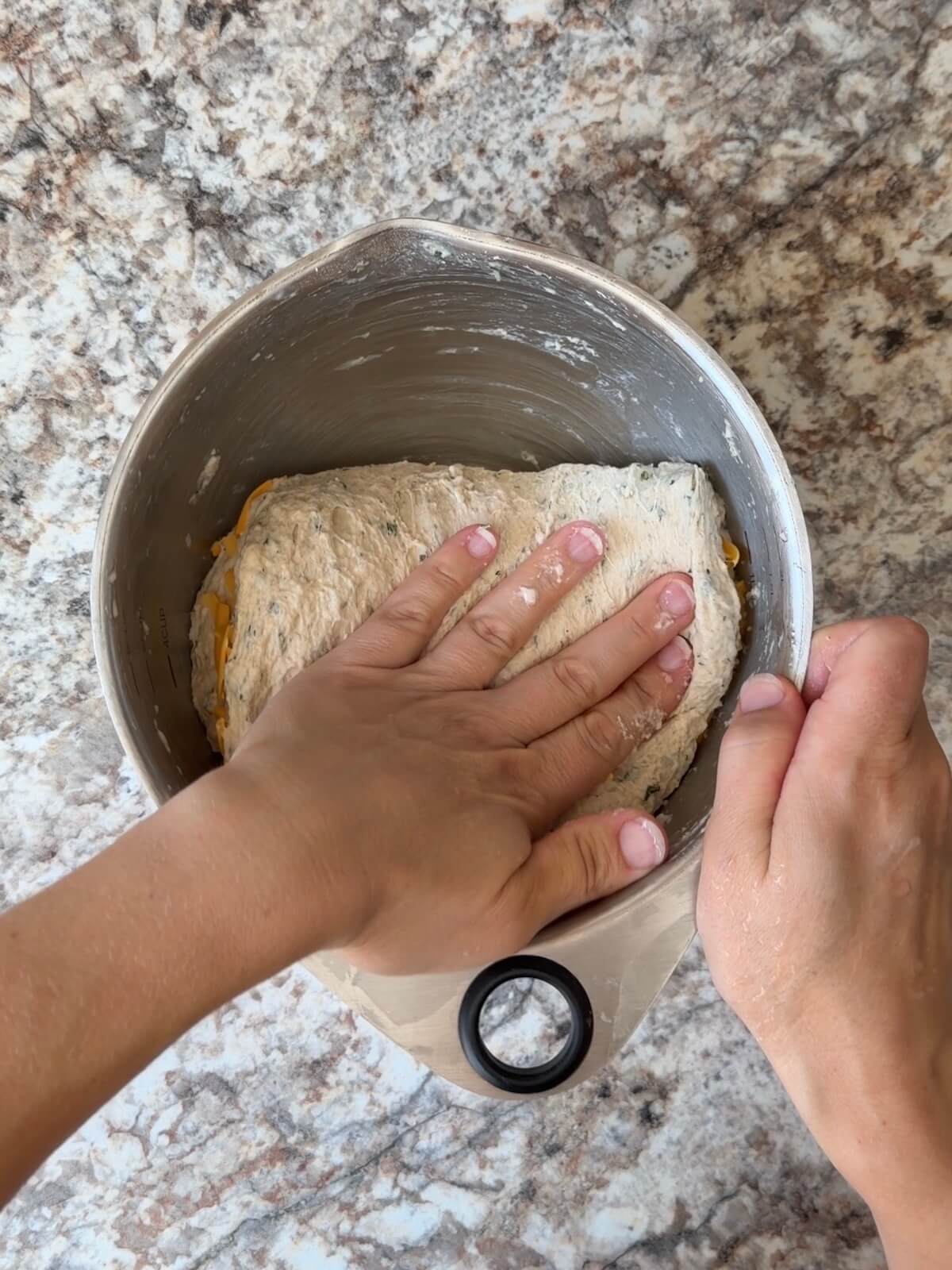 Shredded cheddar cheese being folded into the dough.