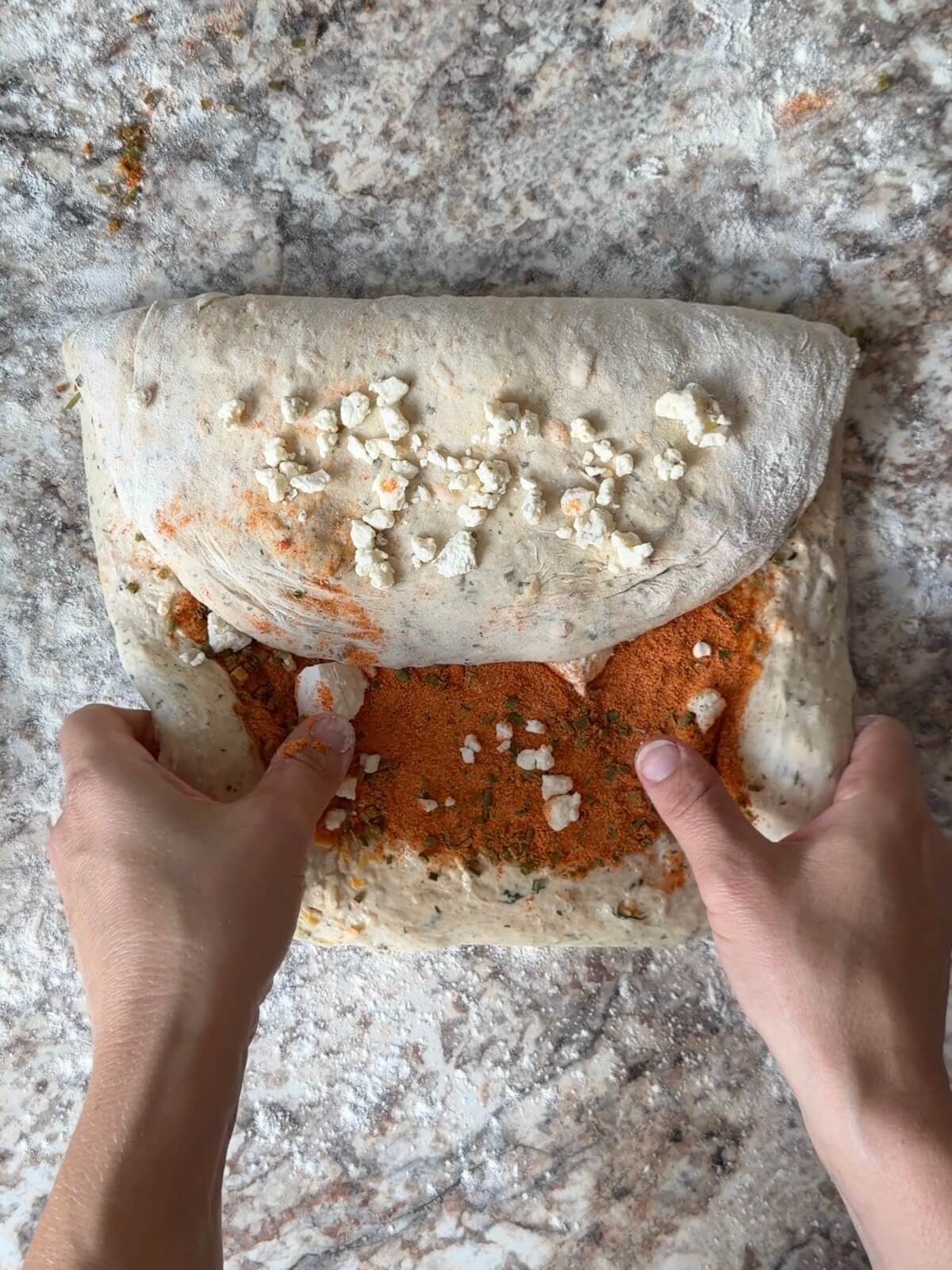 Two hands shaping buffalo chicken sourdough bread dough on a floured counter.