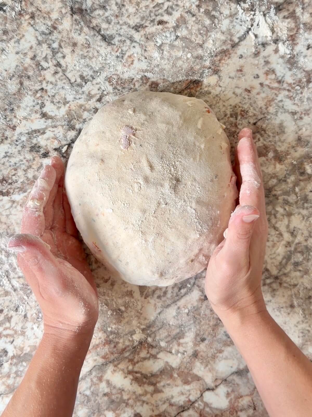 Pepperoni pizza sourdough bread being shaped into a round dough ball.