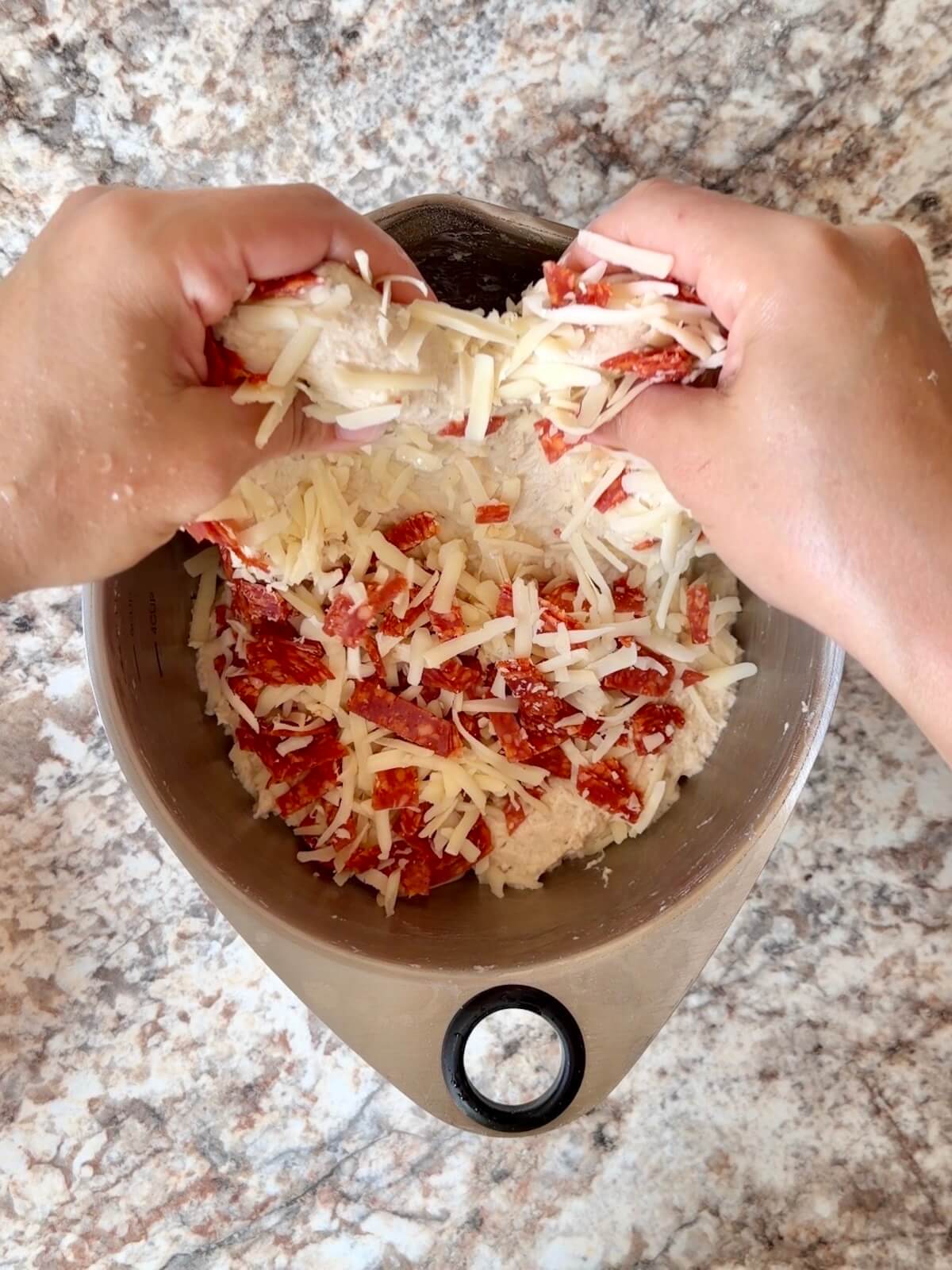 Pepperoni, mozzarella, and parmesan cheese being stretched and folded into the dough.