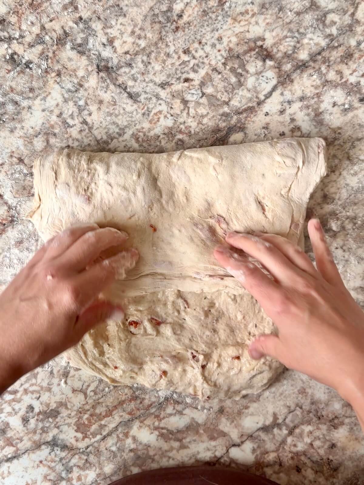 Sourdough pizza bread dough being shaped on a floured counter.