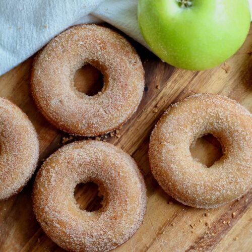 Sourdough apple cider donuts on a wooden cutting board with a whole green apple.
