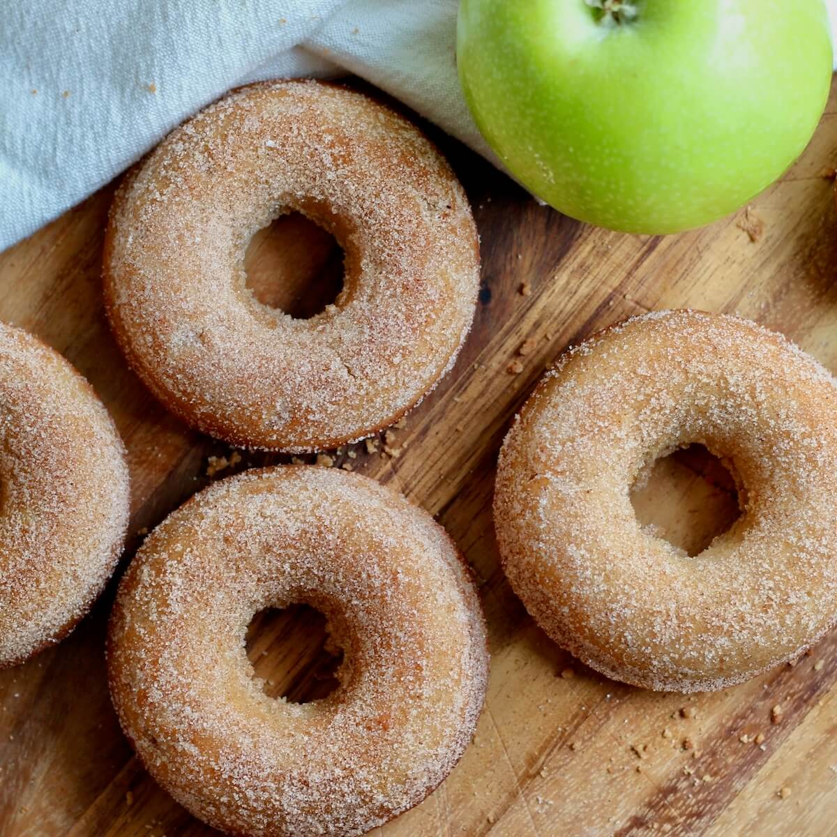 Sourdough apple cider donuts on a wooden cutting board with a whole green apple.