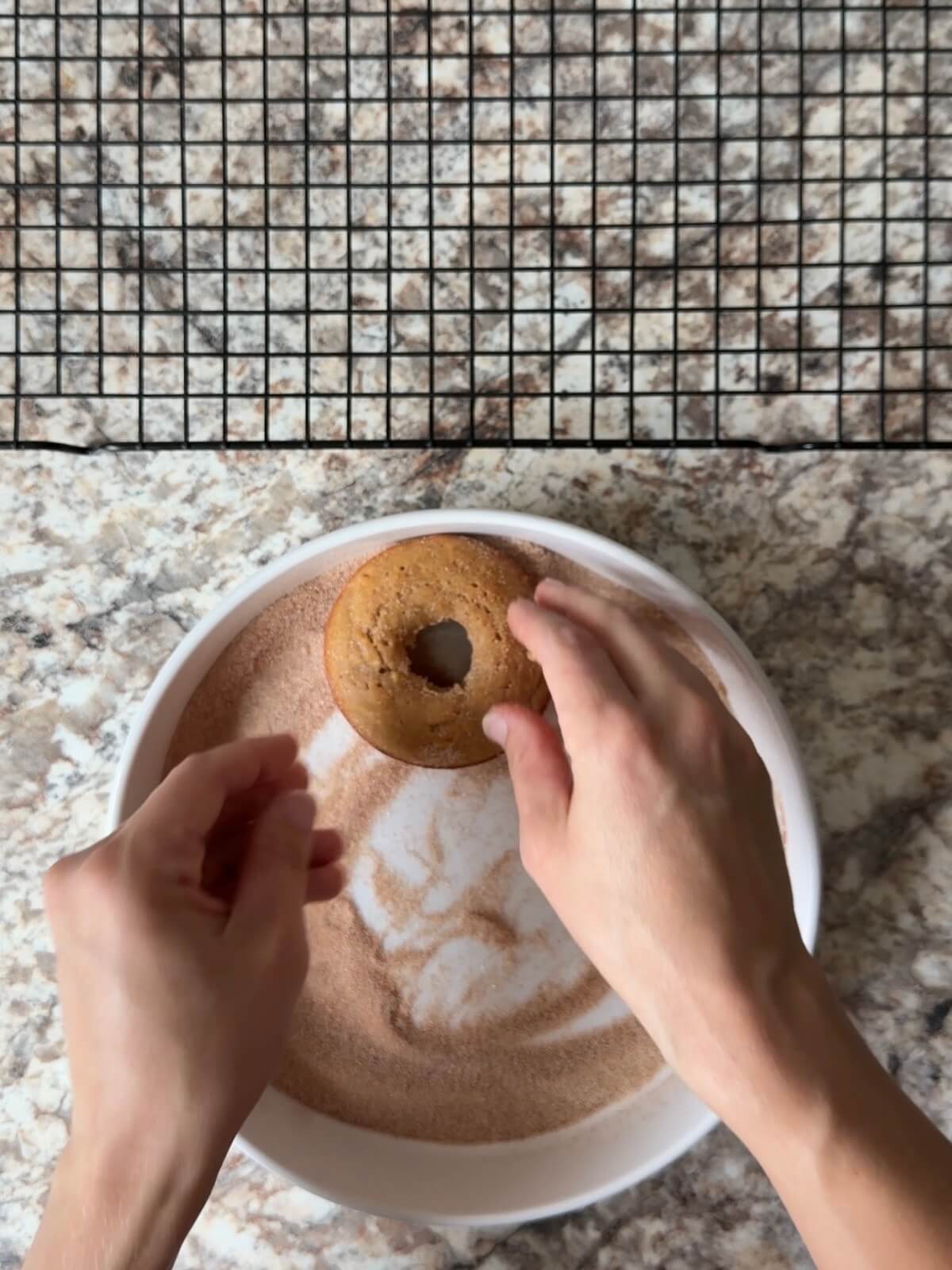A baked sourdough apple cider donut being dipped in a mixture of cinnamon sugar.