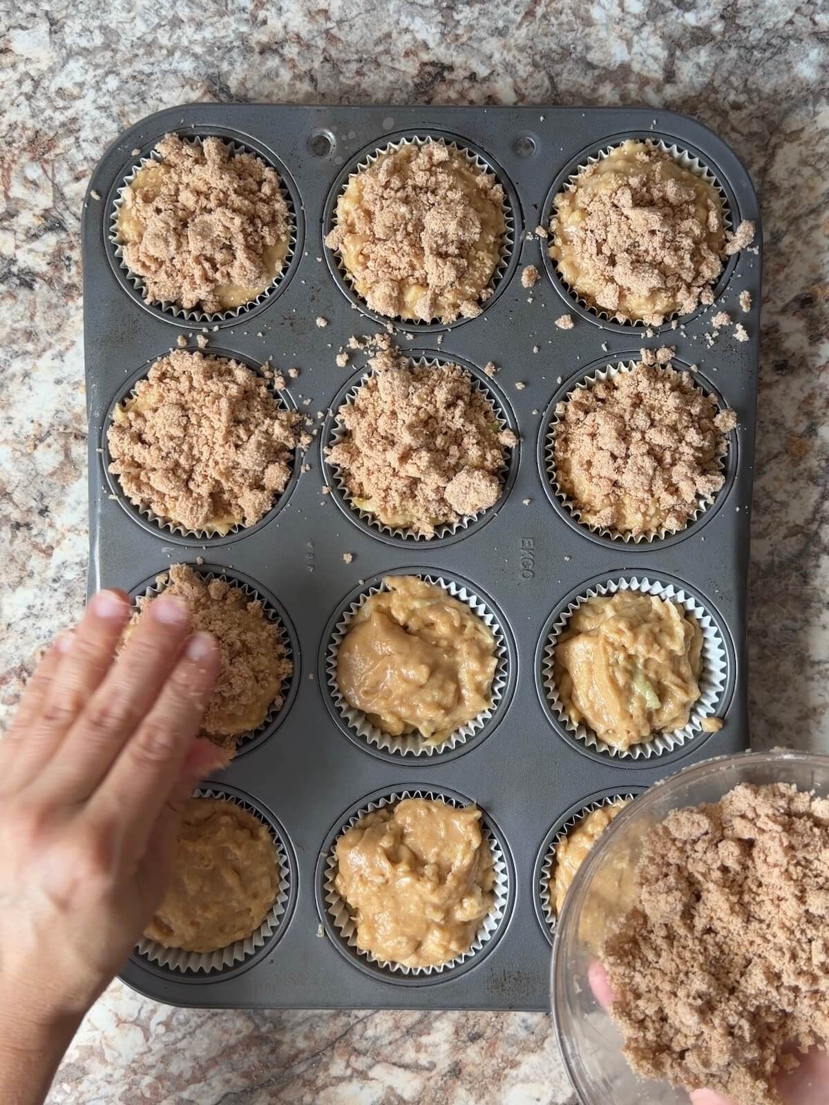 Cinnamon streusel topping being sprinkled on top of the apple muffin batter.