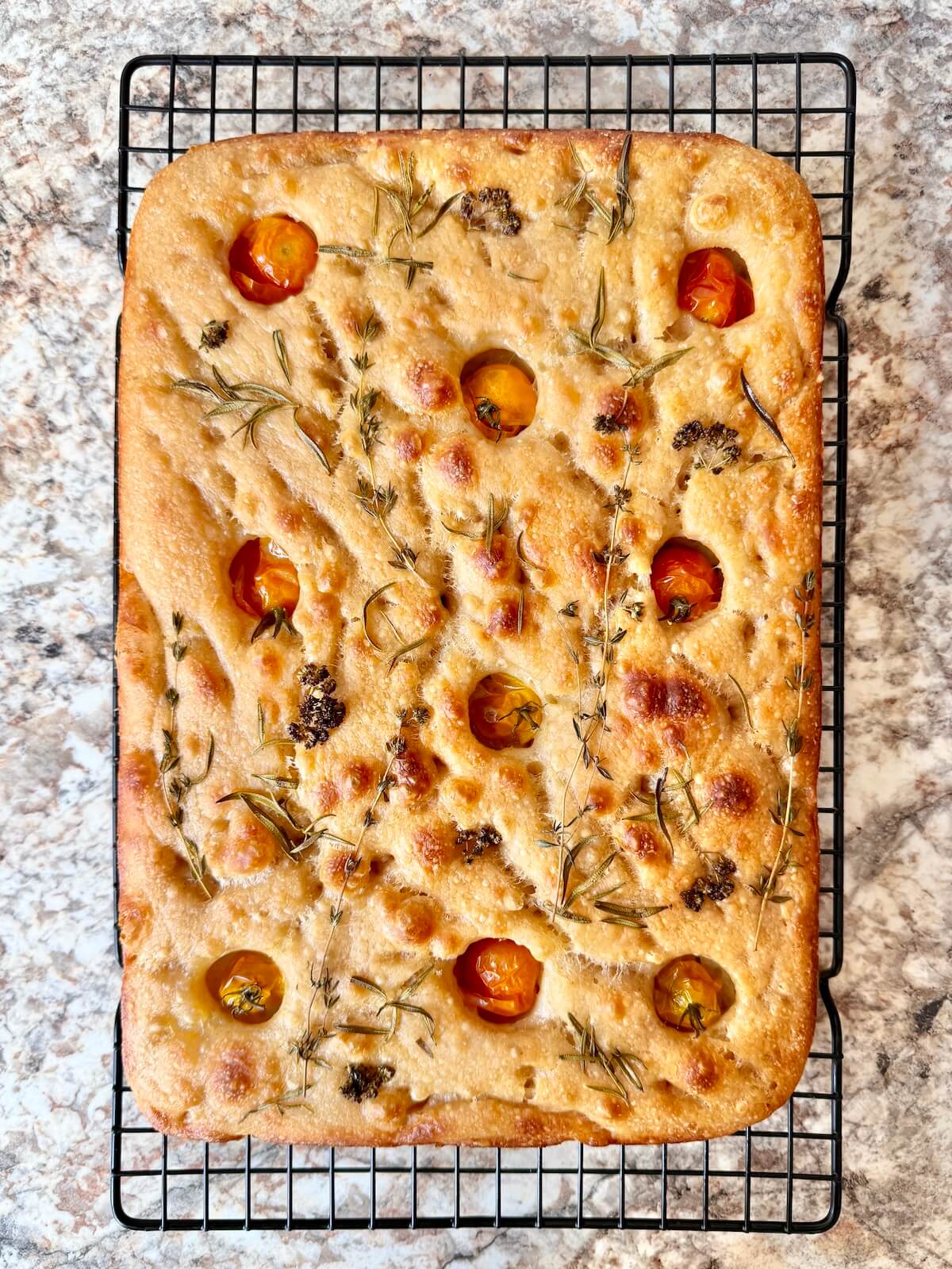 Baked sourdough discard focaccia bread with herbs and tomatoes on a wire cooling rack.