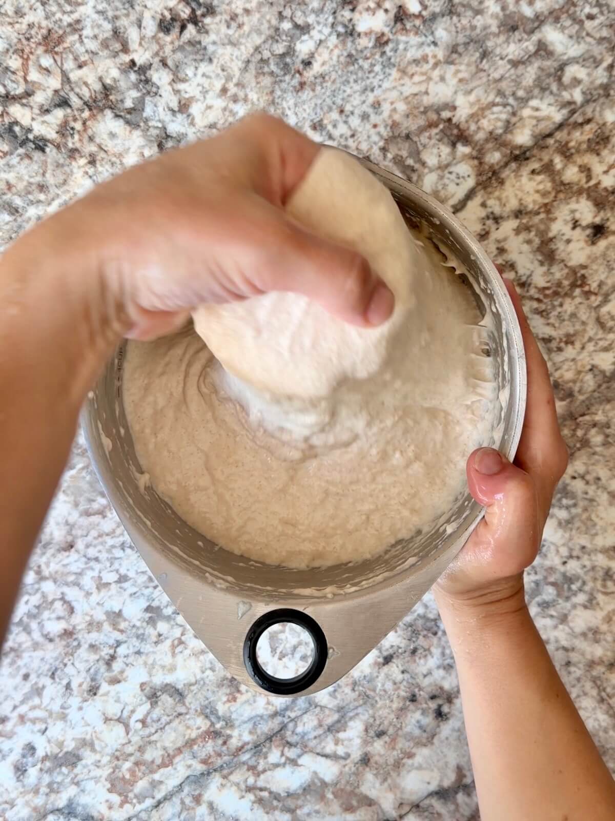 Two hands stretching and folding sourdough focaccia bread dough.