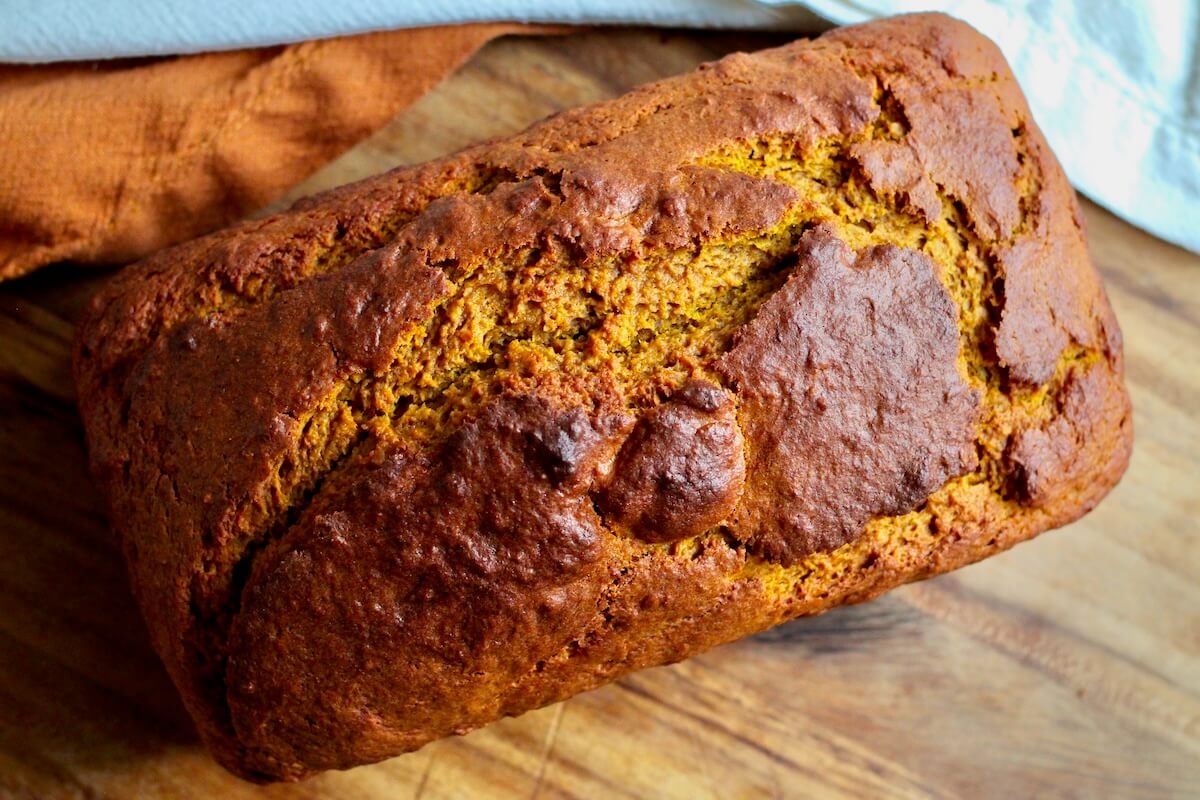 A whole, uncut loaf of sourdough pumpkin quick bread on a wooden cutting board.