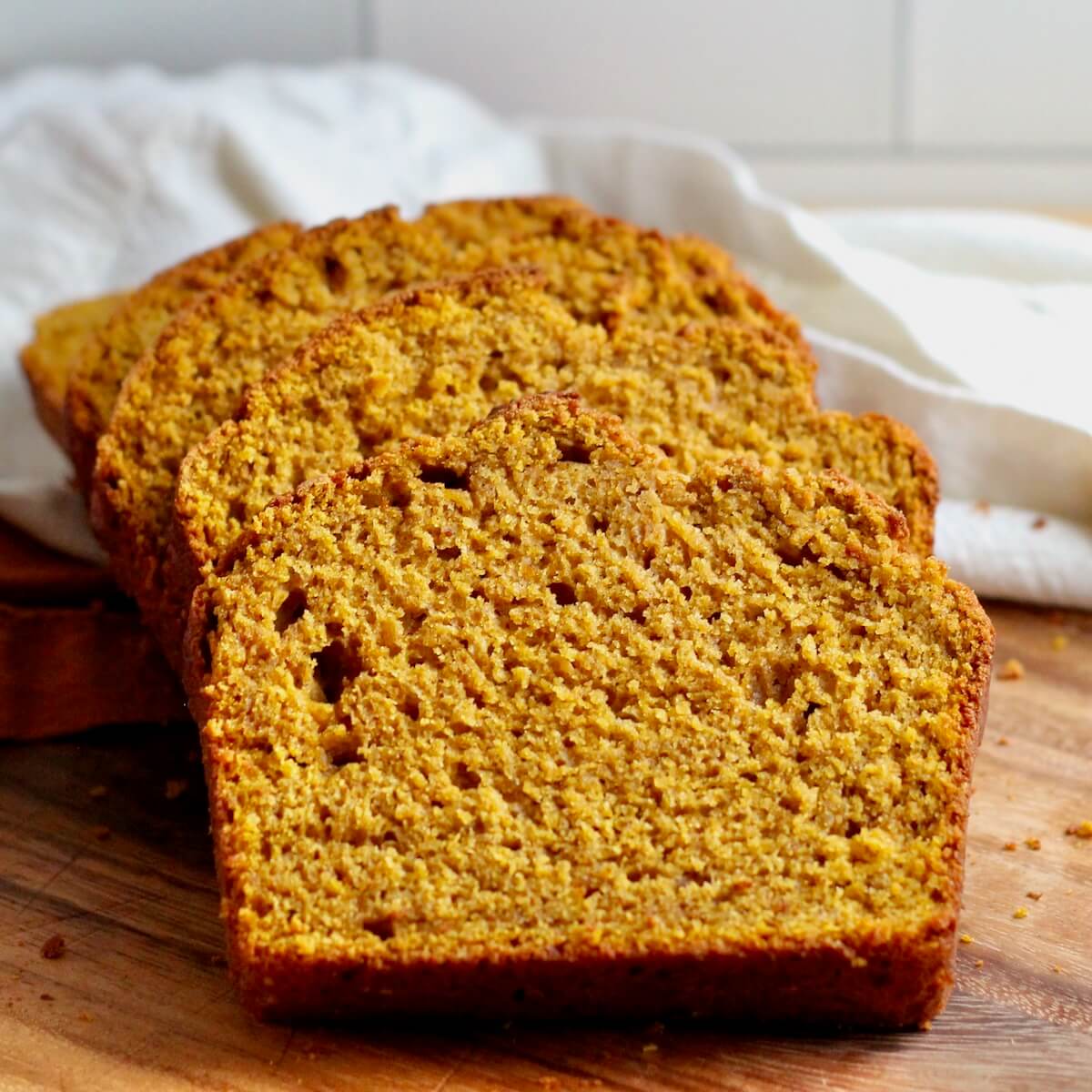 Slices of sourdough discard pumpkin bread on a wooden cutting board with white and orange cloth napkins in the background.