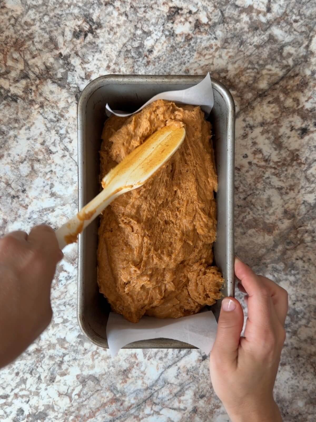 Sourdough pumpkin quick bread batter being spread into a parchment-lined loaf pan.