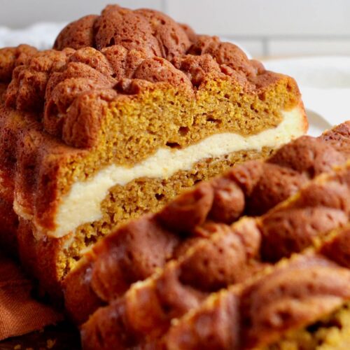 A loaf of sourdough pumpkin cream cheese bread. Half of the loaf is cut into slices.