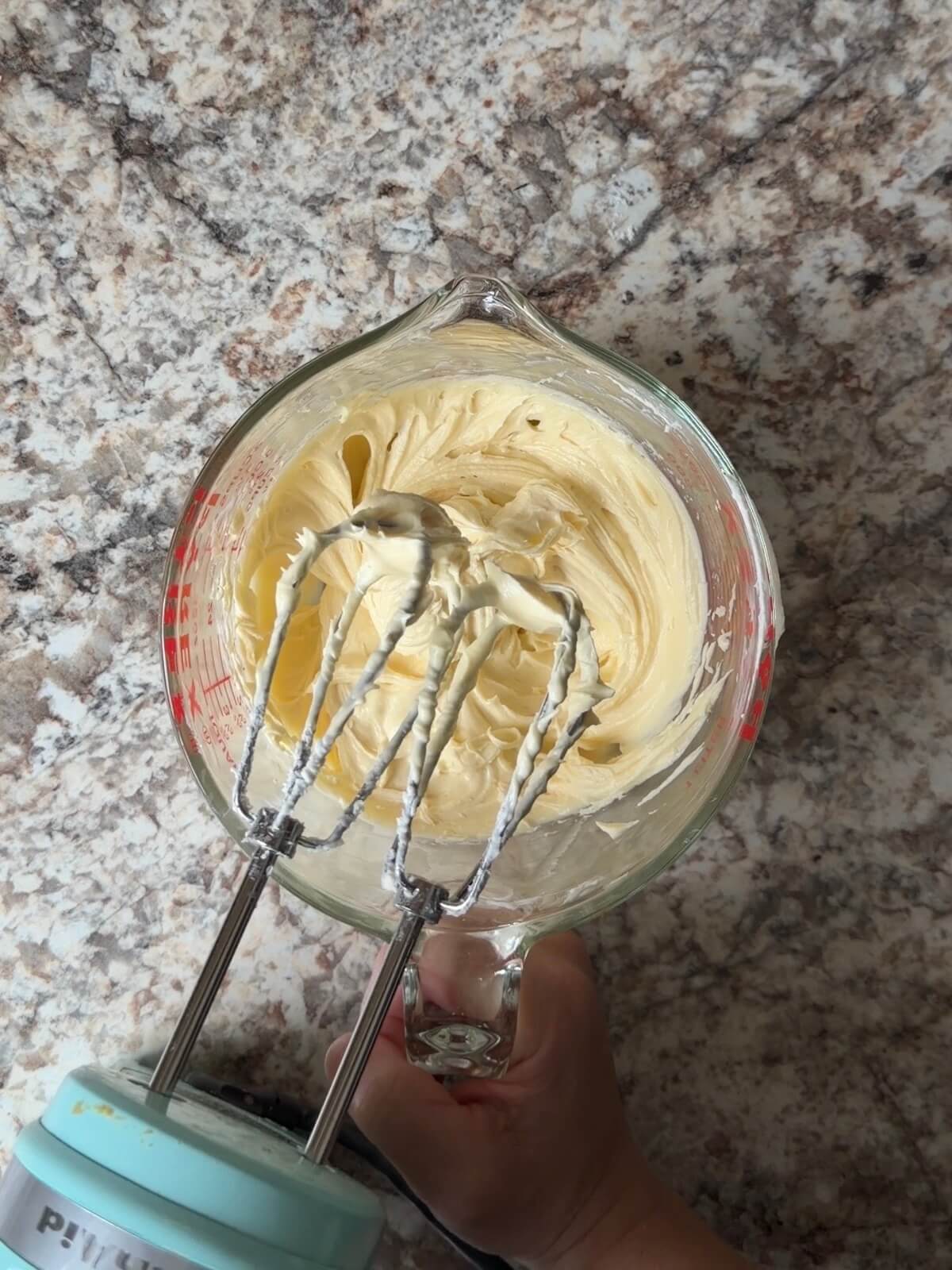 The cream cheese layer mixed together in a large glass measuring cup. The hand mixer is resting over the bowl.
