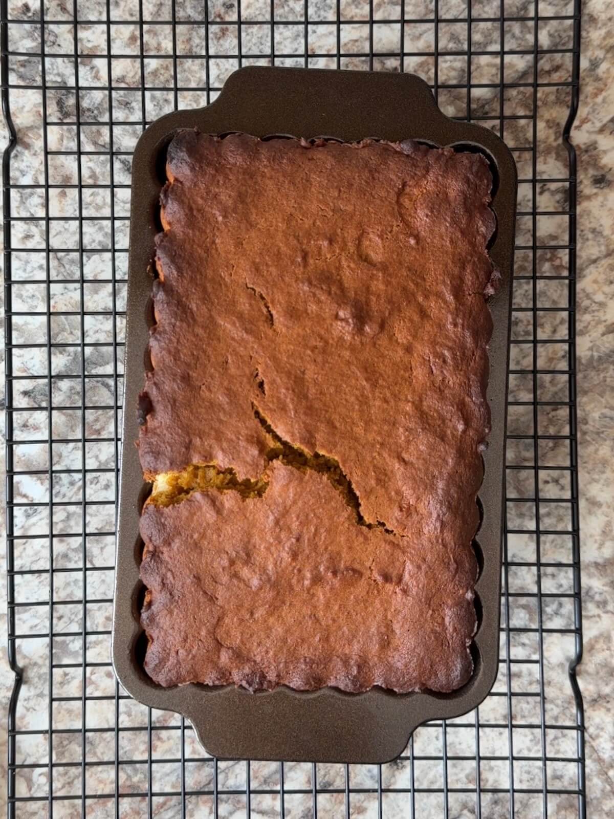 A baked loaf of sourdough pumpkin cream cheese bread still in the loaf pan on a wire cooling rack.