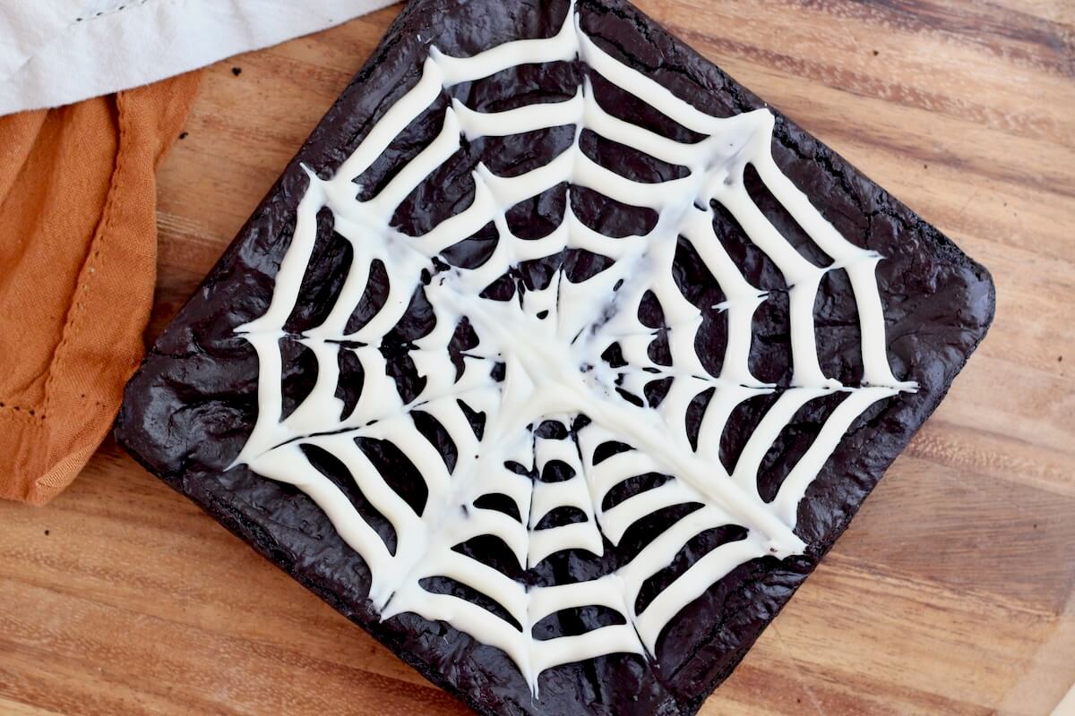 A square of sourdough black cocoa brownies with a cream cheese frosting spider web design on top.