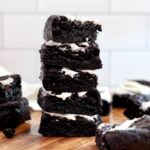 A stack of five black cocoa sourdough brownies with cream cheese frosting.