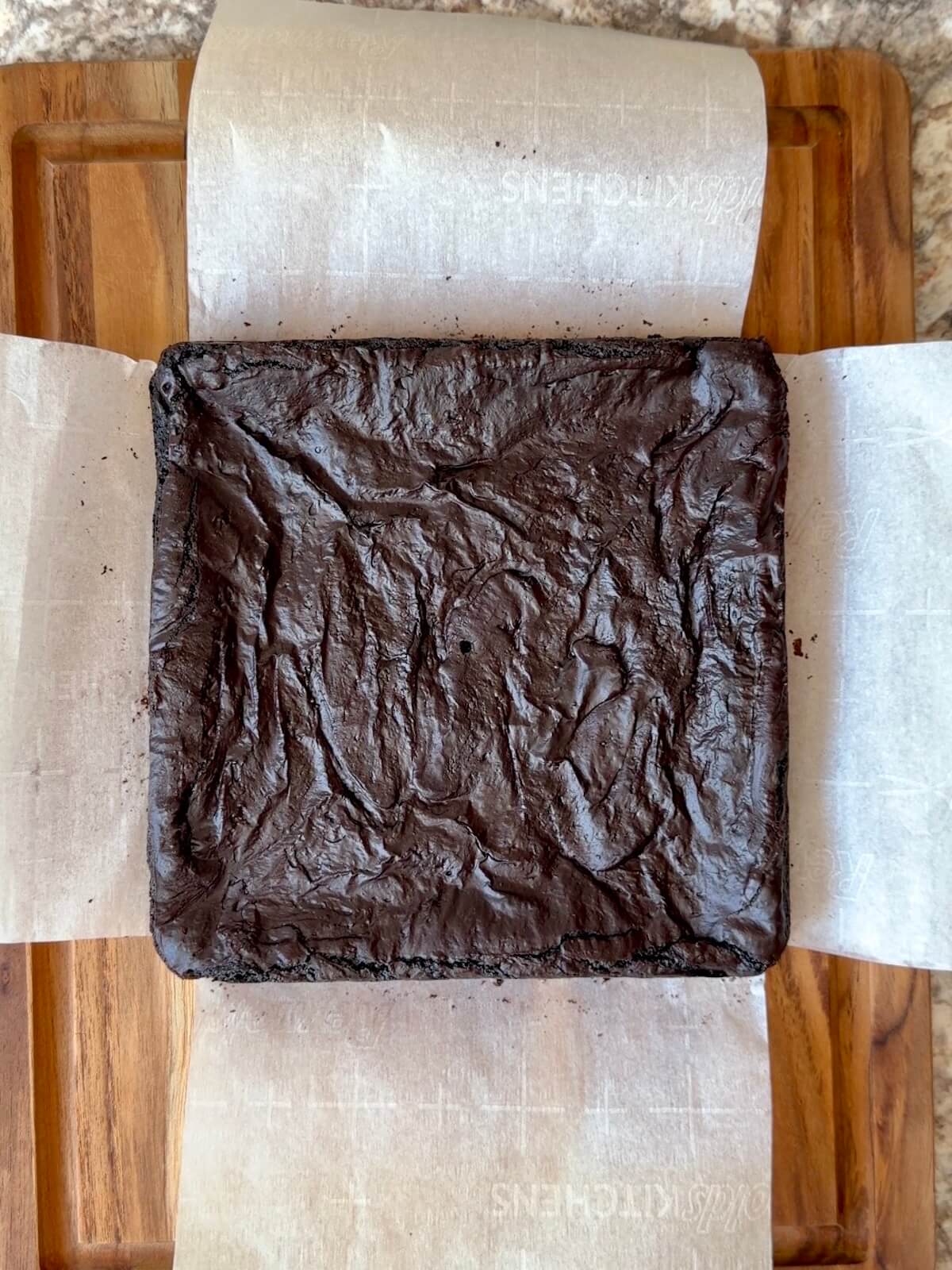 Baked black cocoa sourdough brownies on a wooden cutting board before being cut.