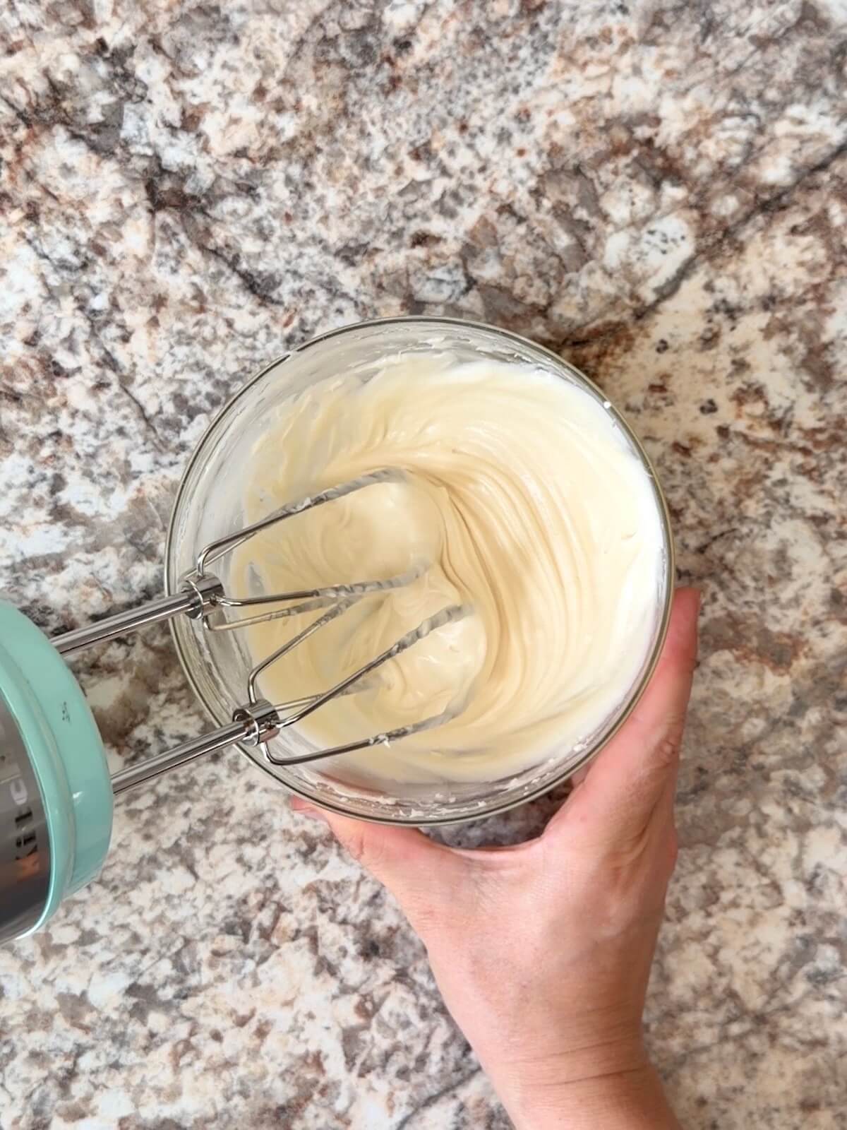 Cream cheese frosting being mixed with a hand mixer in a small bowl.