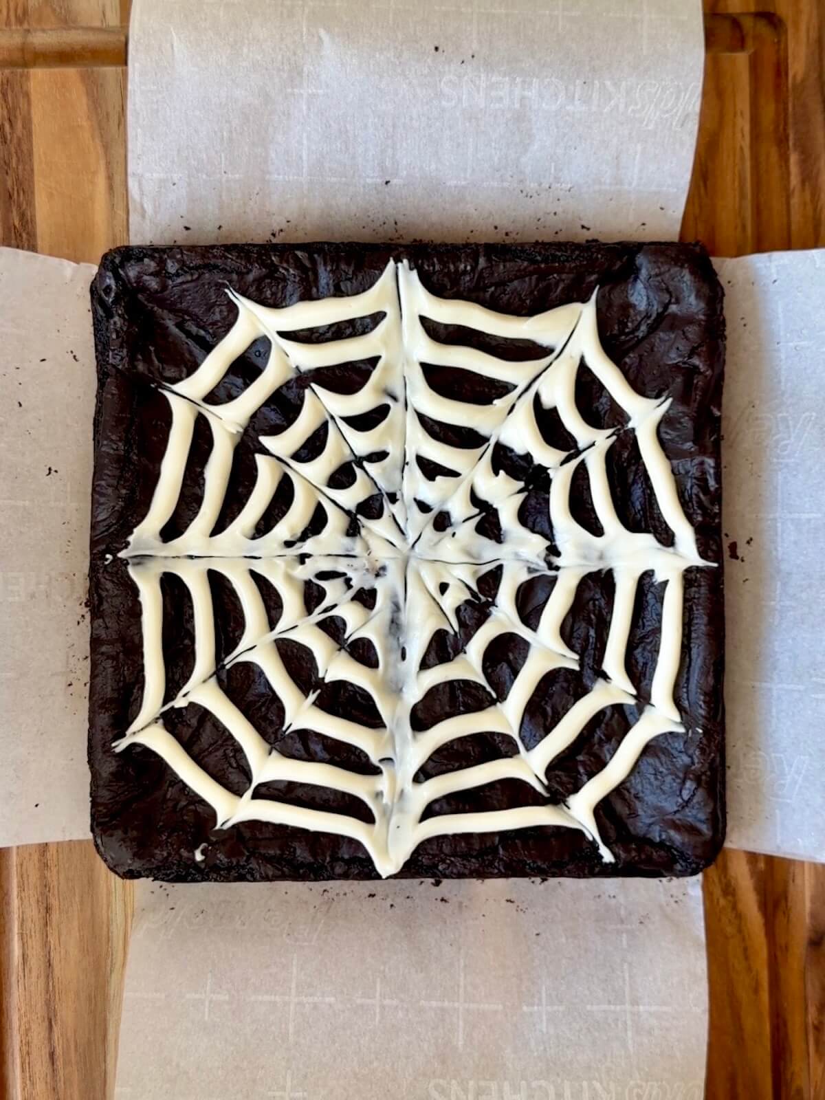 Black cocoa sourdough brownies with a cream cheese frosting spider web on top.