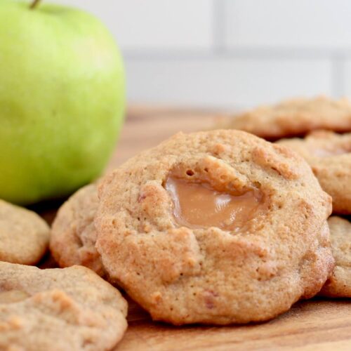 Several caramel apple sourdough cookies on a cutting board with a fresh green apple out of focus in the background.